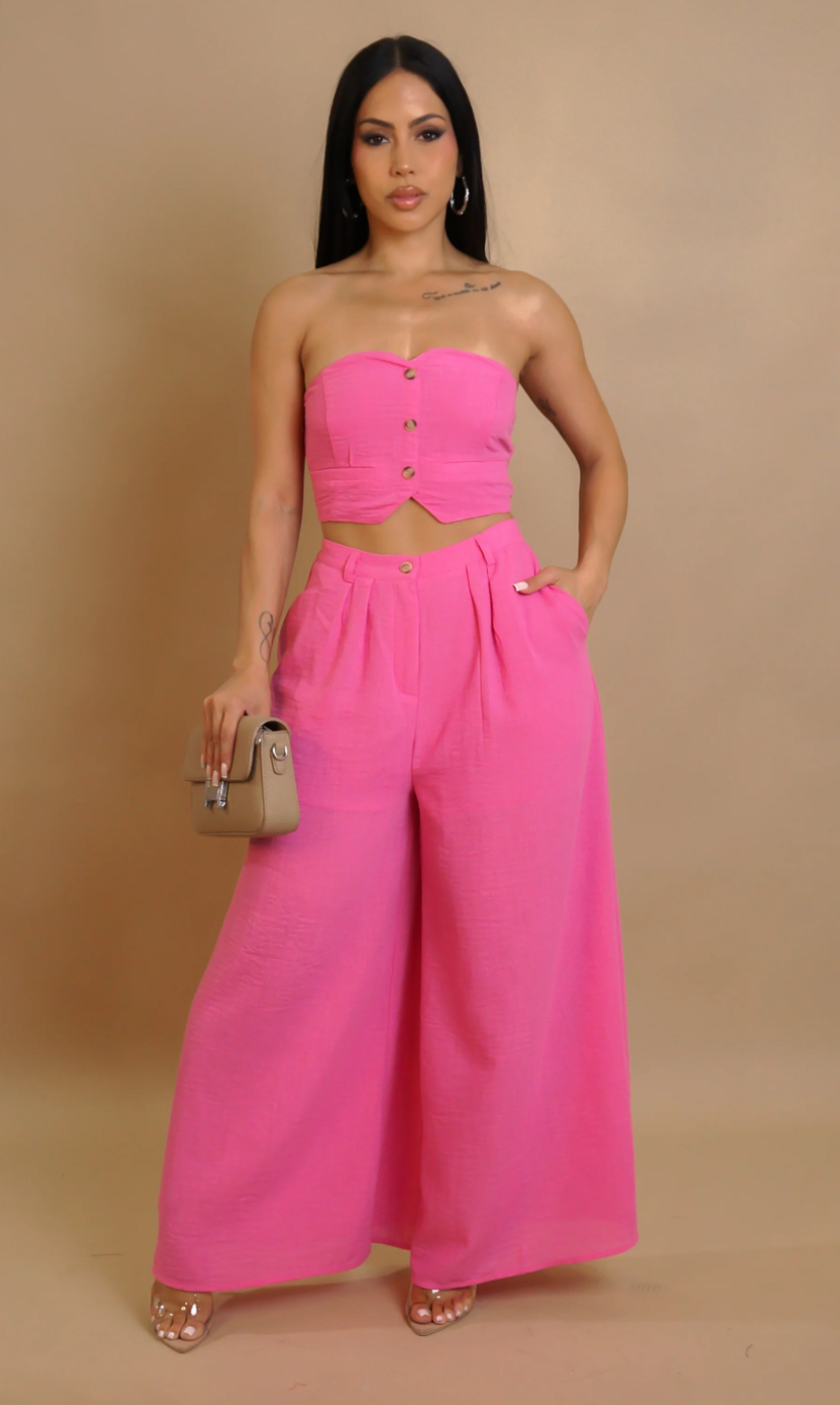 Woman wearing a bright pink strapless top and wide-leg pants against a beige background