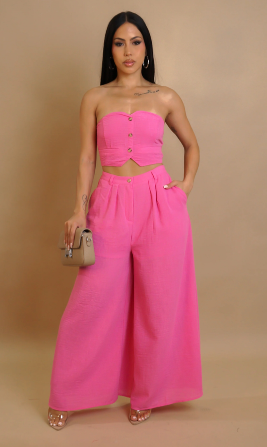 Woman wearing a bright pink strapless top and wide-leg pants against a beige background